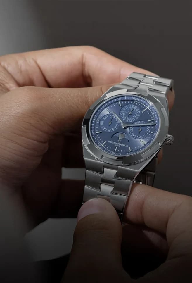 A hand holding a steel watch with a blue perpetual-calendar dial