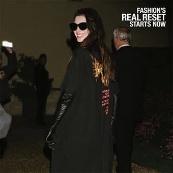A woman in sunglasses and a black coat at a night-time fashion event
